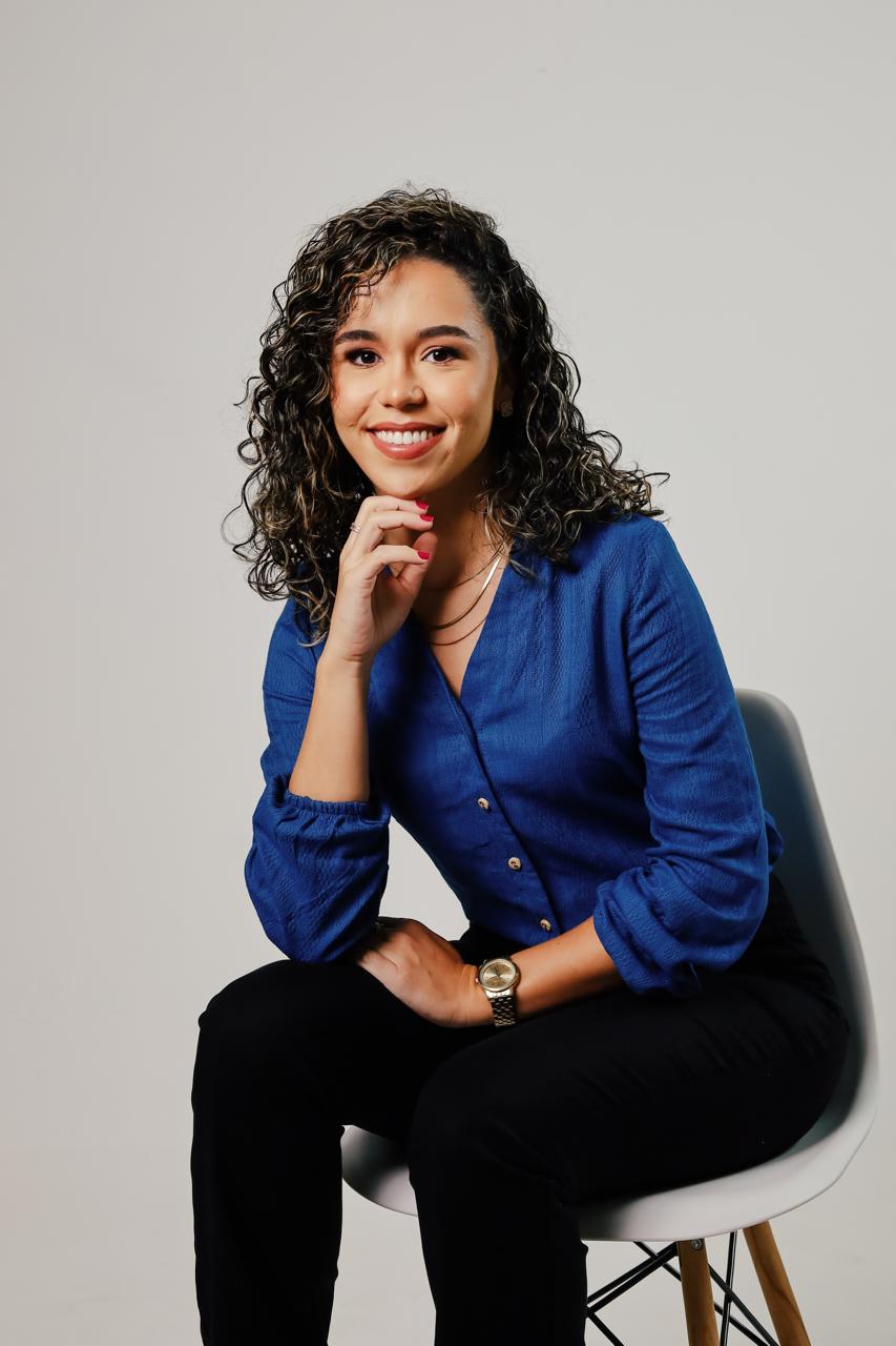 Jessiane Cunha sentada, com a mão no queixo, sorrindo
